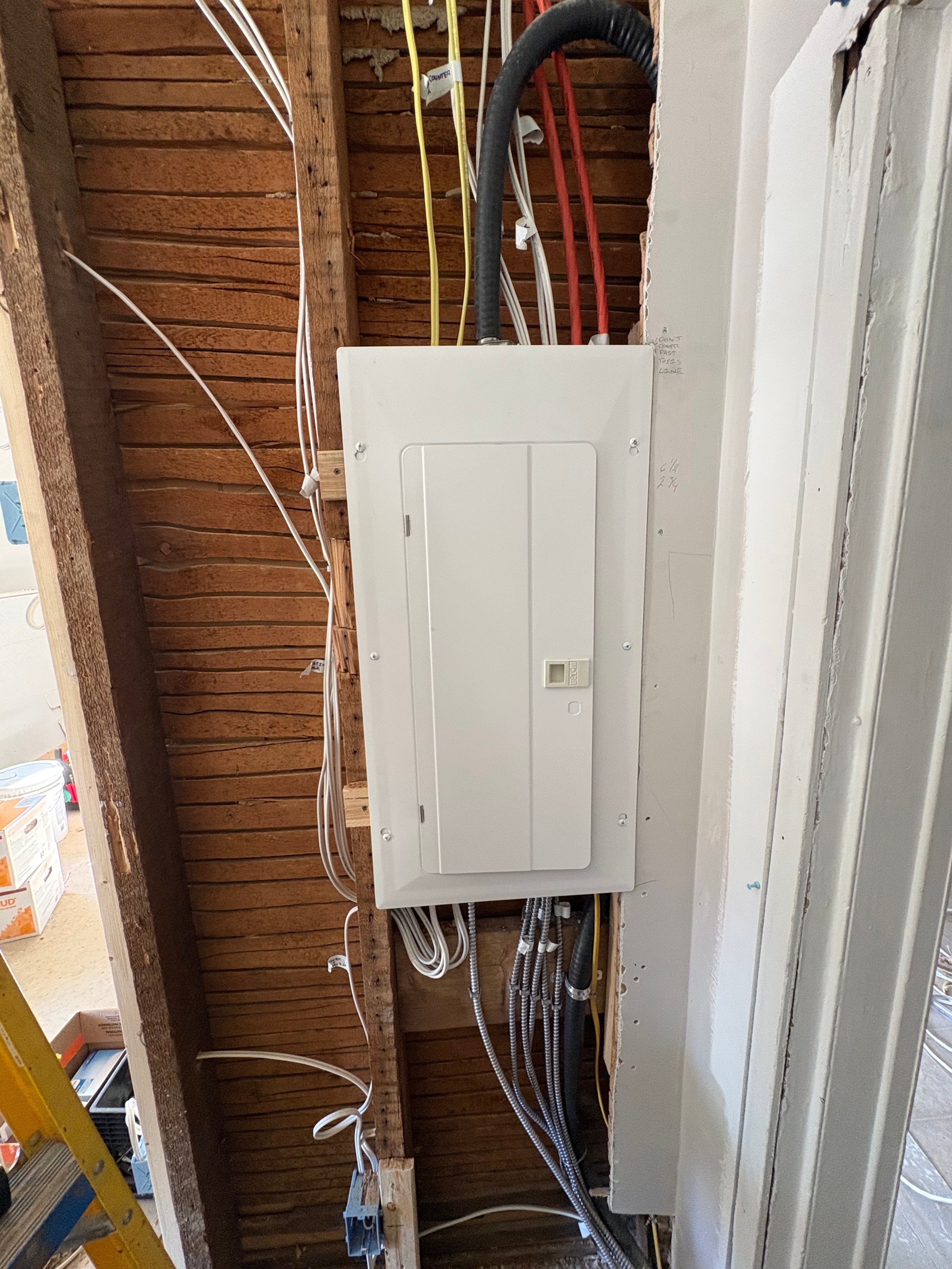 New electrical panel installed in open wall framing with branch-circuit cables and armoured conduit runs visible on both sides, Smiths Falls home rewire
